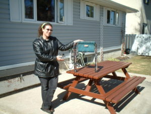 Lady standing next to a picnic table in back yard with her camp seat